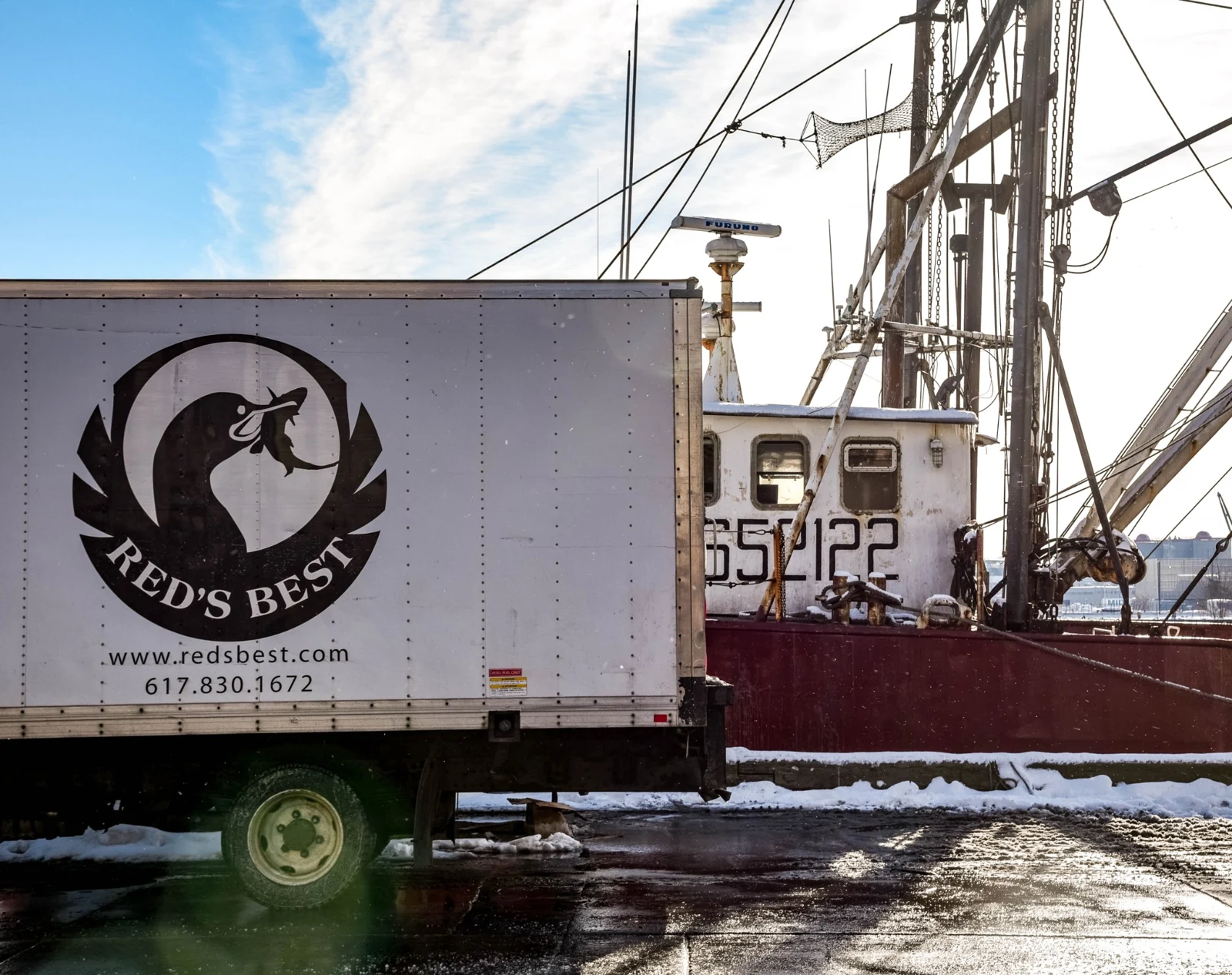 A Red’s Best seafood truck parked alongside a working fishing boat