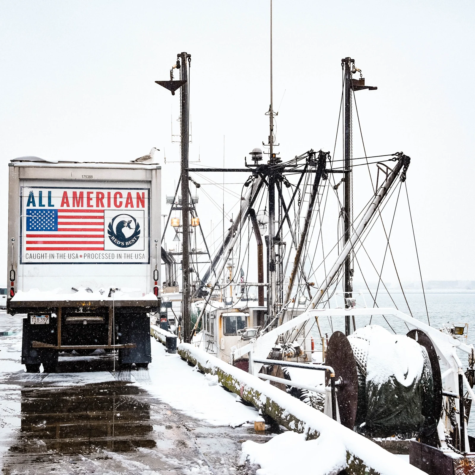 A Red’s Best truck beside fishing boats at a snow-covered dock