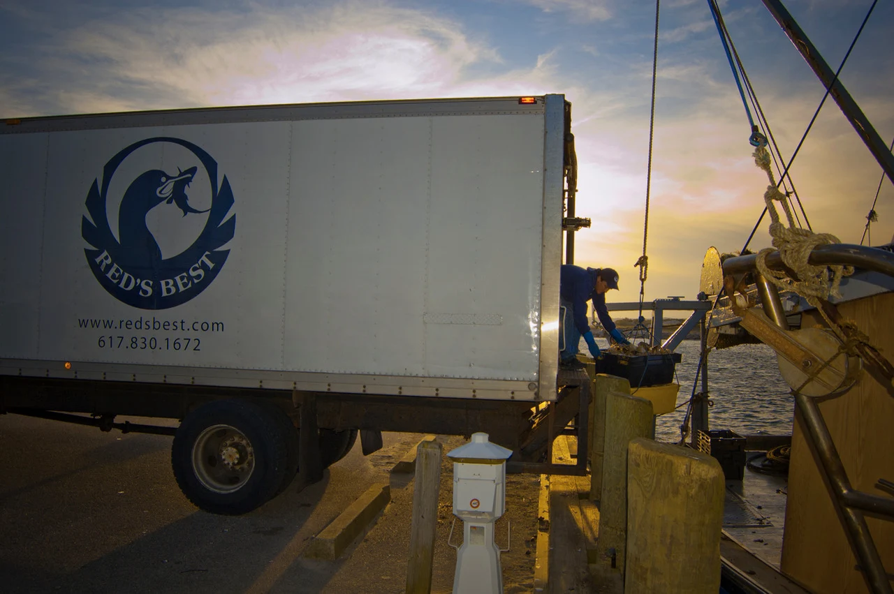 Red’s Best truck and team member beside a fishing boat at sunset